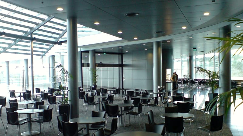 A short institutional hallway with numbered solid doors, each with a narrow slot, under continuous ceiling lighting.