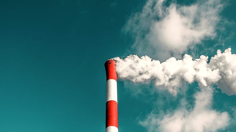 Two tall steel stacks rising above a low industrial building, with a clear pale sky behind them.