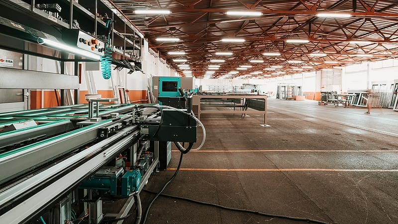 Workers in blue coveralls and hard hats crossing a factory floor past a line of machines and stacked pallets.