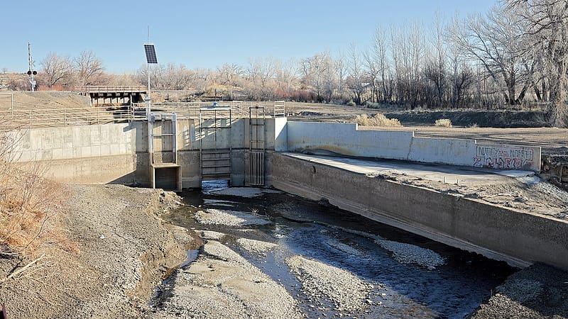 An irrigation canal curving away from a river between two fields, one green and planted, the other bare dirt.
