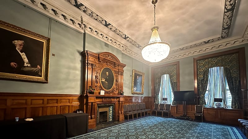 An empty institutional room with a plain table, two chairs facing each other and a closed metal door behind.
