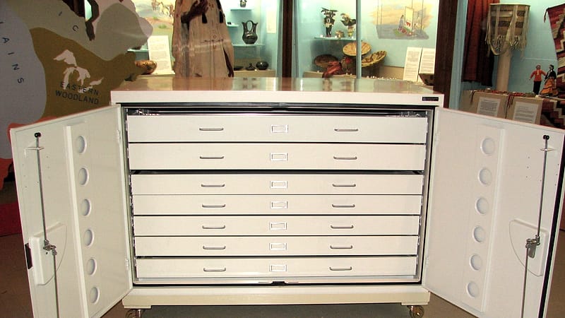 An open metal filing drawer packed with tabbed manila folders, one pulled forward under an office lamp.