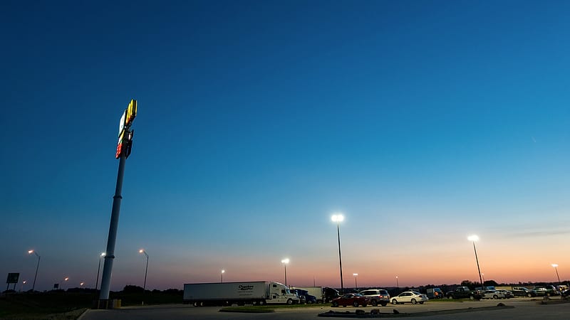 A sleeper tractor with a personalized cab parked at a truck stop beside a fuel island at first light.