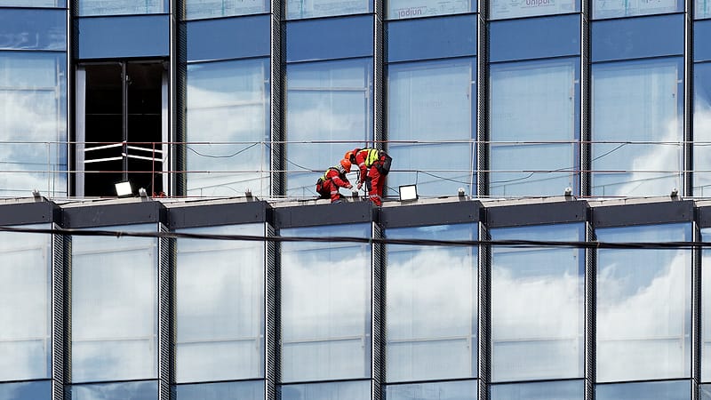 A partly built steel frame on a construction site with two crews working on separate levels under a pale sky.