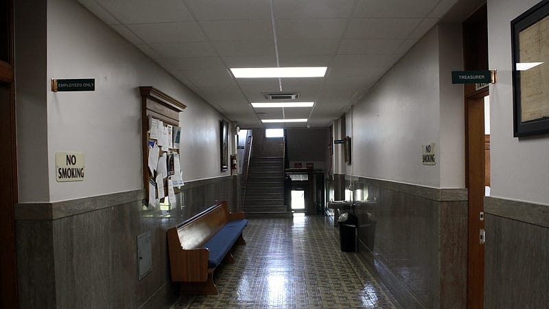 A small waiting area with fixed plastic chairs, a service window and a clipboard resting on a low counter.
