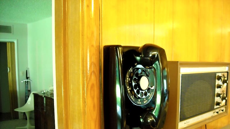 A row of wall-mounted payphones in a painted concrete corridor with short metal cords and no seating.
