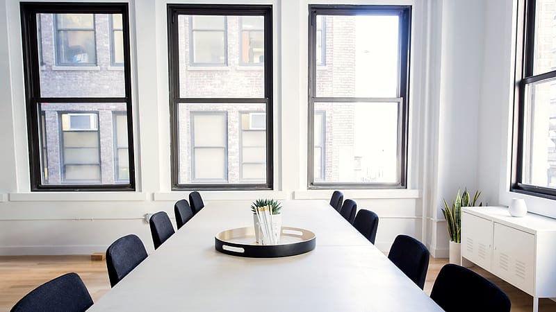 Two chairs facing each other across a narrow table in a bare meeting room with a closed door behind.