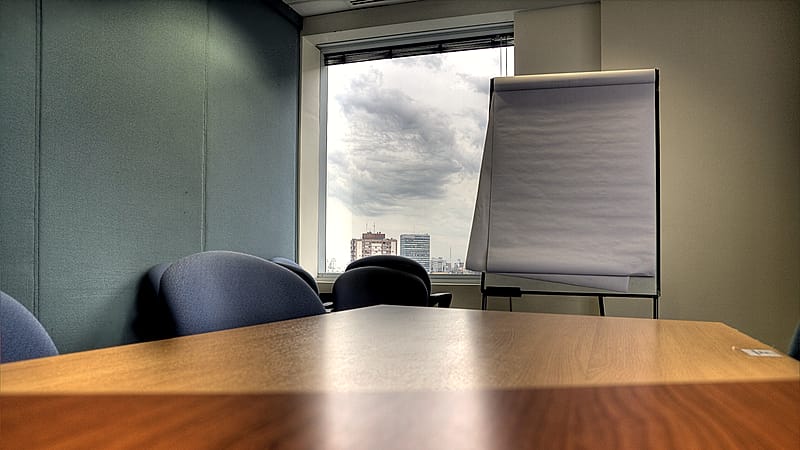 A long conference table with two rows of chairs facing each other, notepads and water glasses set at each place.