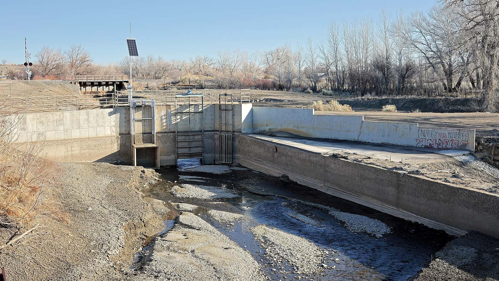 An irrigation canal curving away from a river between two fields, one green and planted, the other bare dirt.