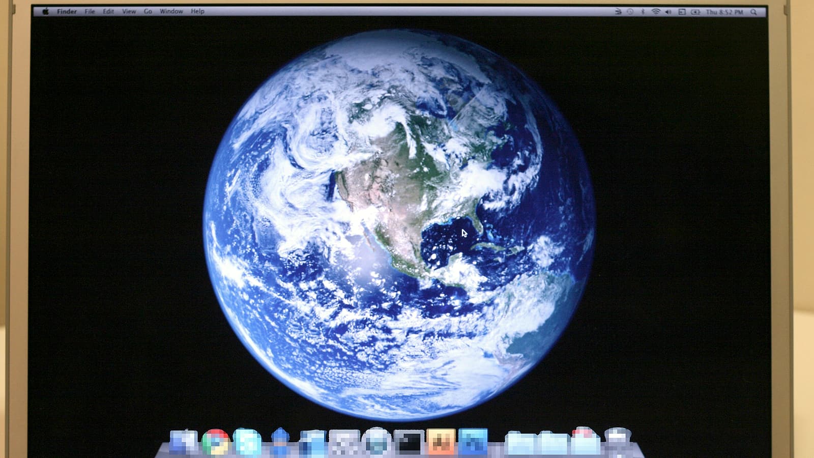 A hand holding a smartphone showing a plain white screen of small text, with a laptop out of focus behind it.