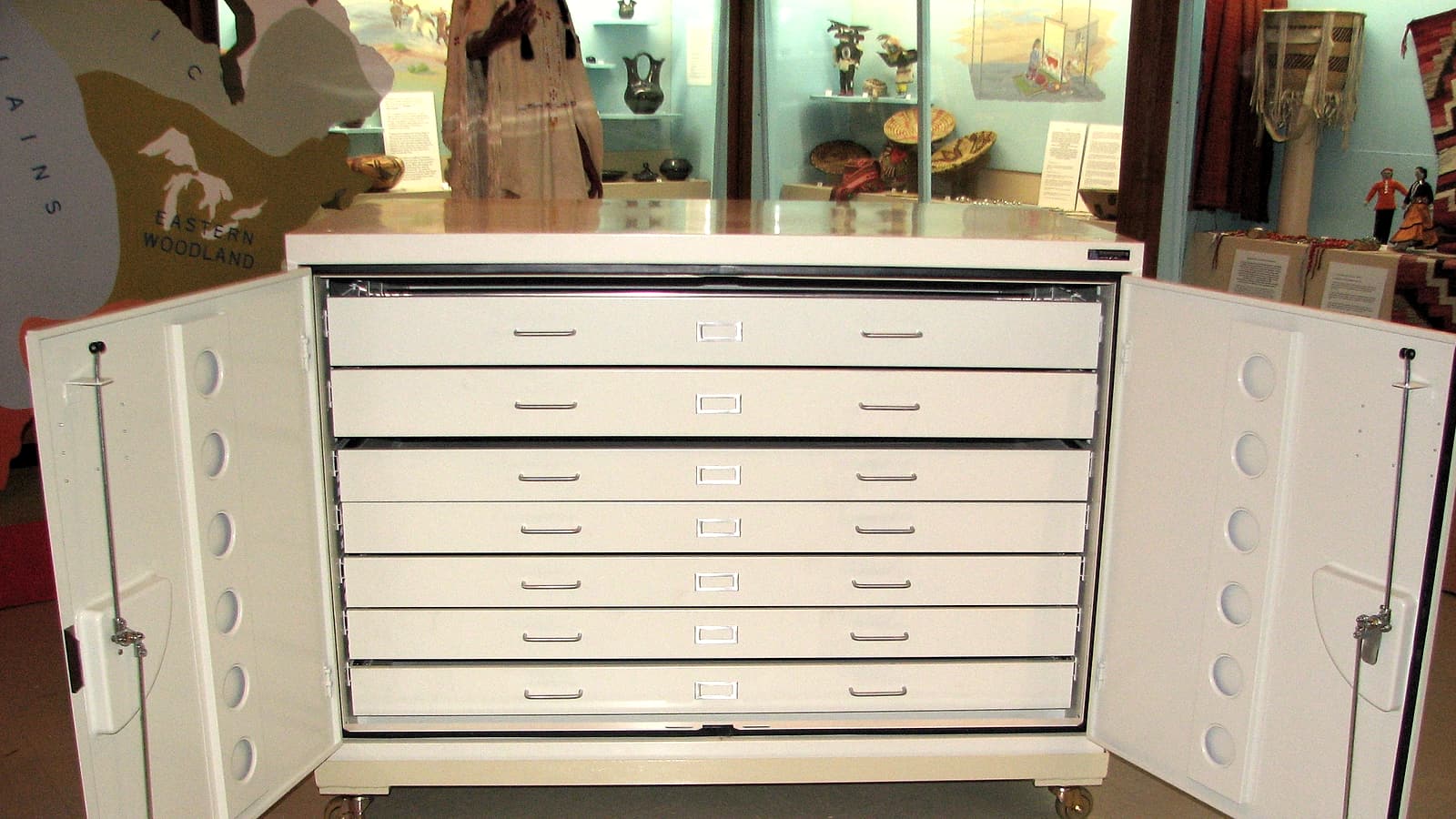 An open metal filing drawer packed with tabbed manila folders, one pulled forward under an office lamp.