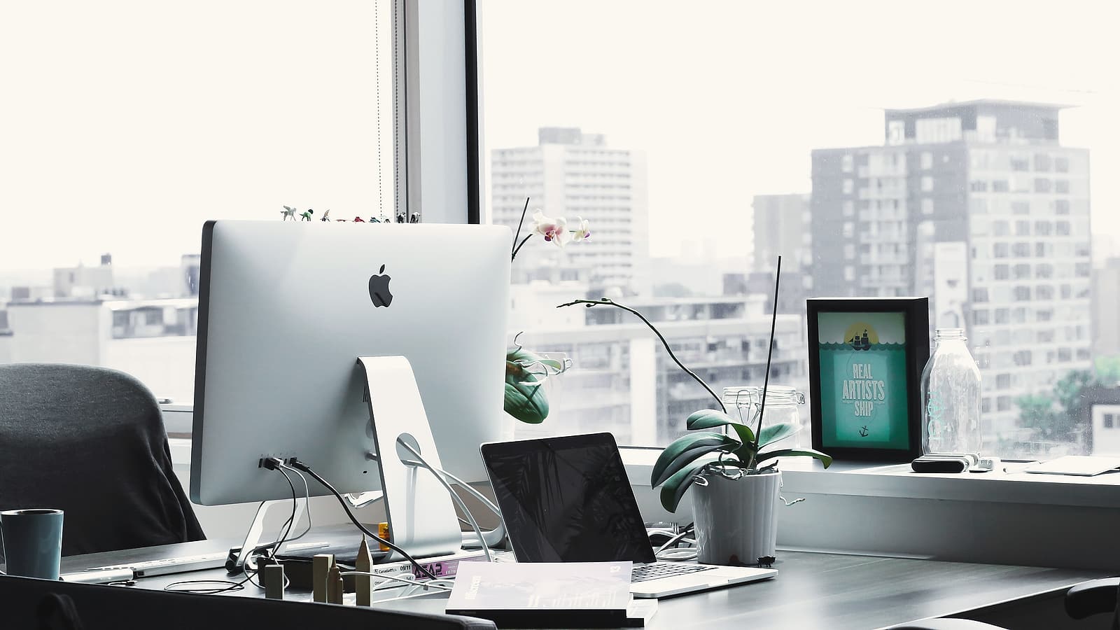 A laptop open on an office table showing a blank sign-in screen, with a coffee cup and a notebook beside it.
