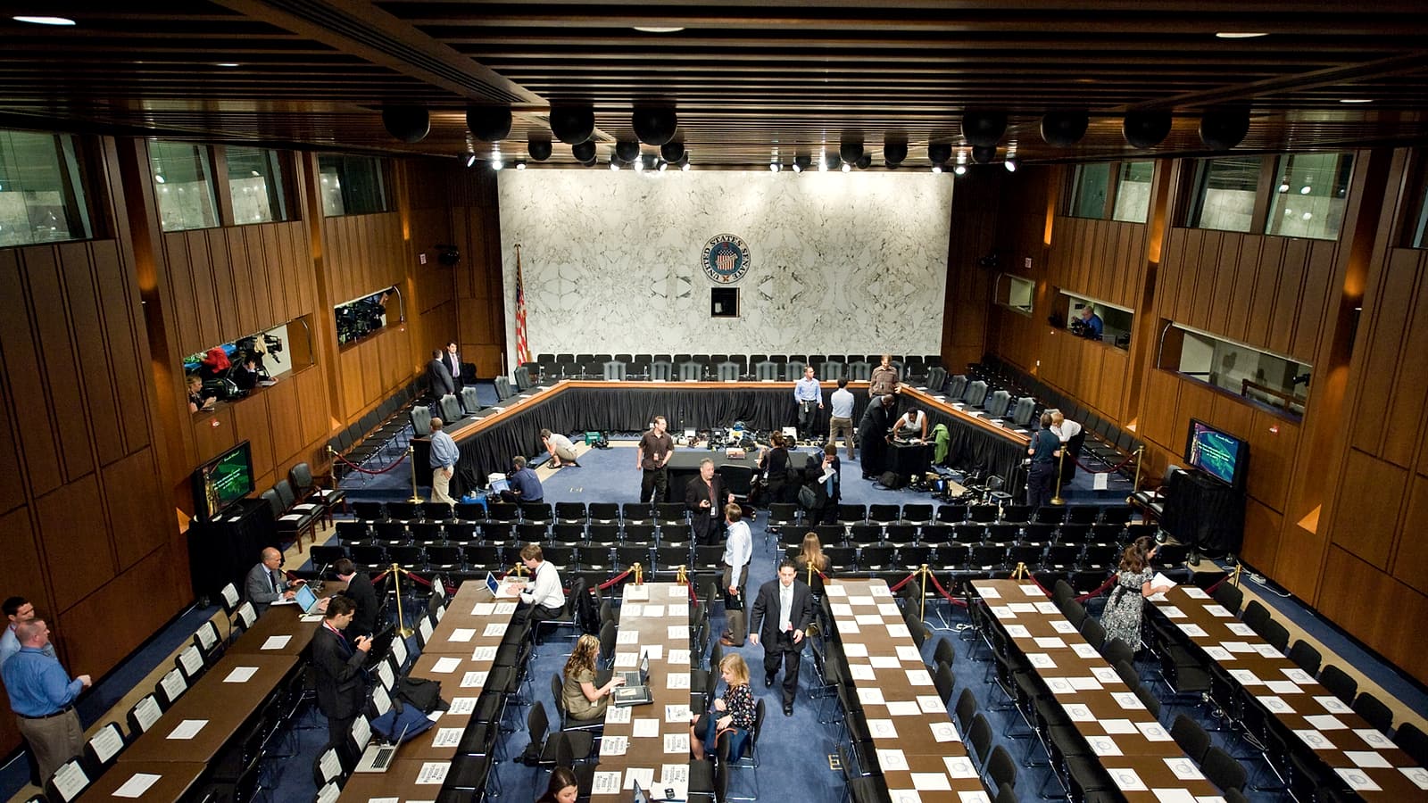 A hearing room with a plain table, a water pitcher, three chairs and a stenographer's machine on a stand.