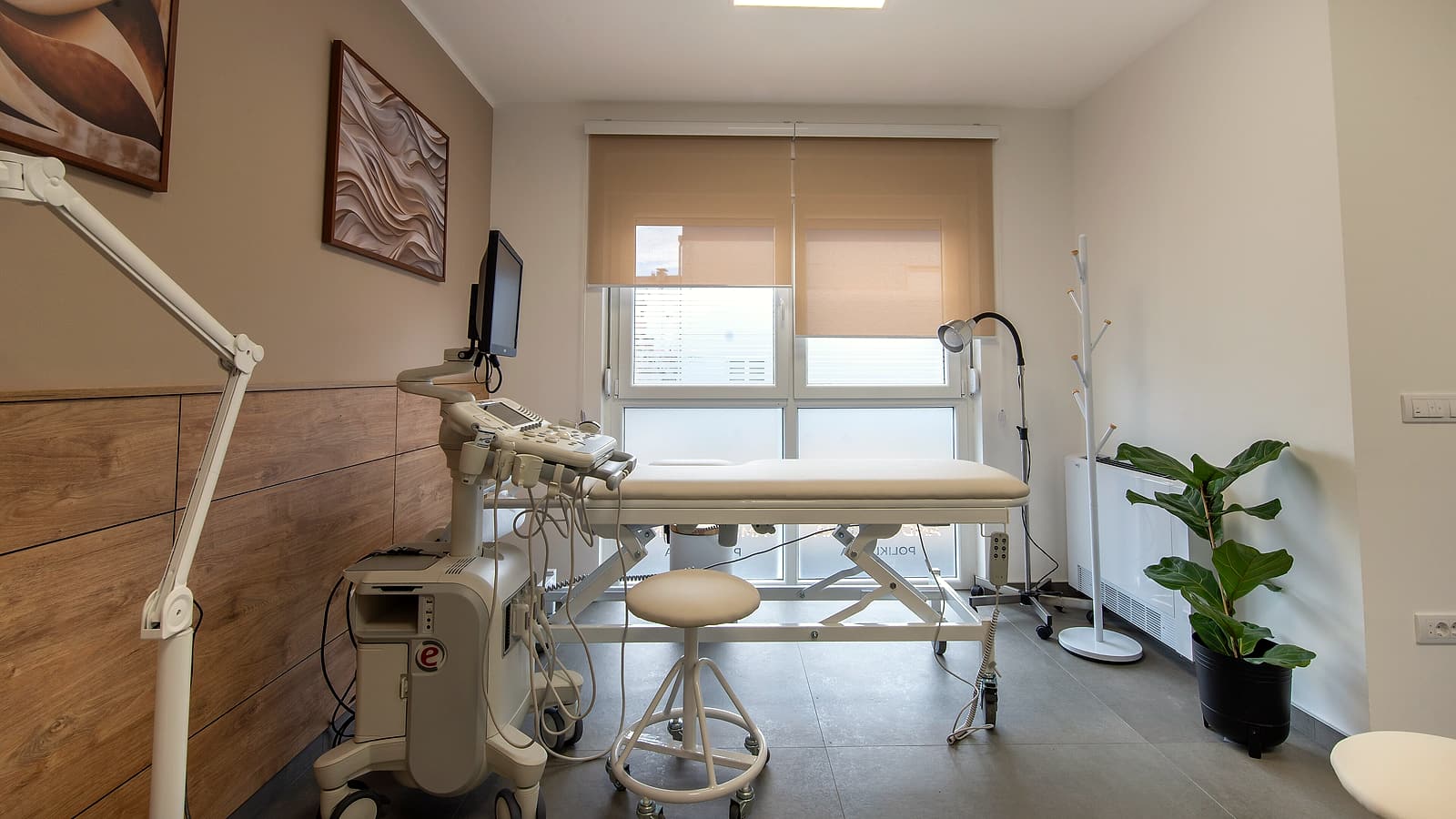 A clinical examination room with a paper-covered table, a blood pressure cuff on the wall and a closed cabinet.