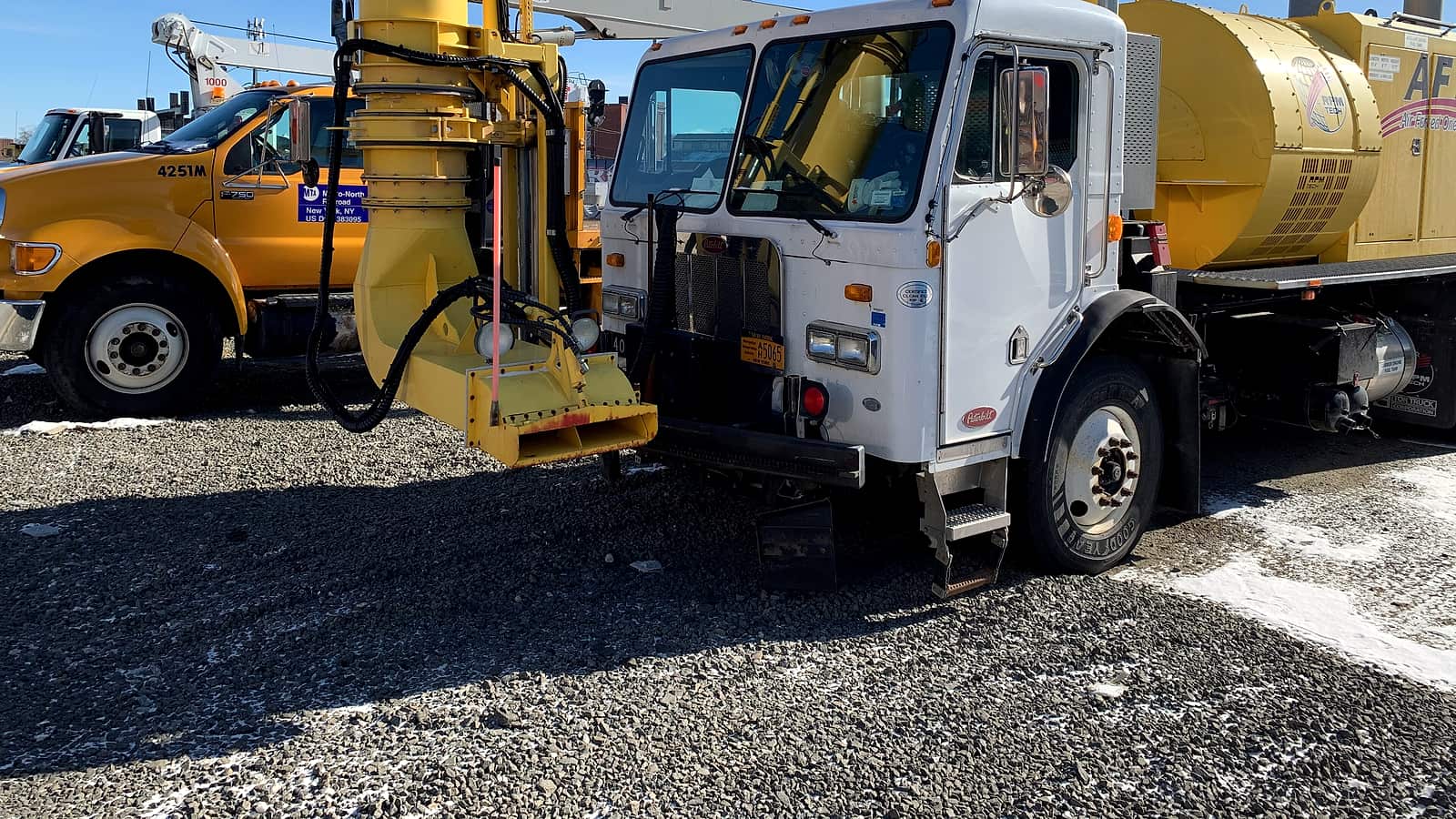 A row of white tractor units parked at angle on asphalt beside a low warehouse with loading bays.