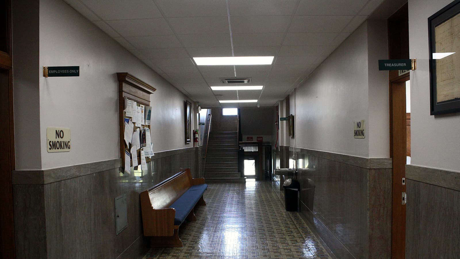 A small waiting area with fixed plastic chairs, a service window and a clipboard resting on a low counter.