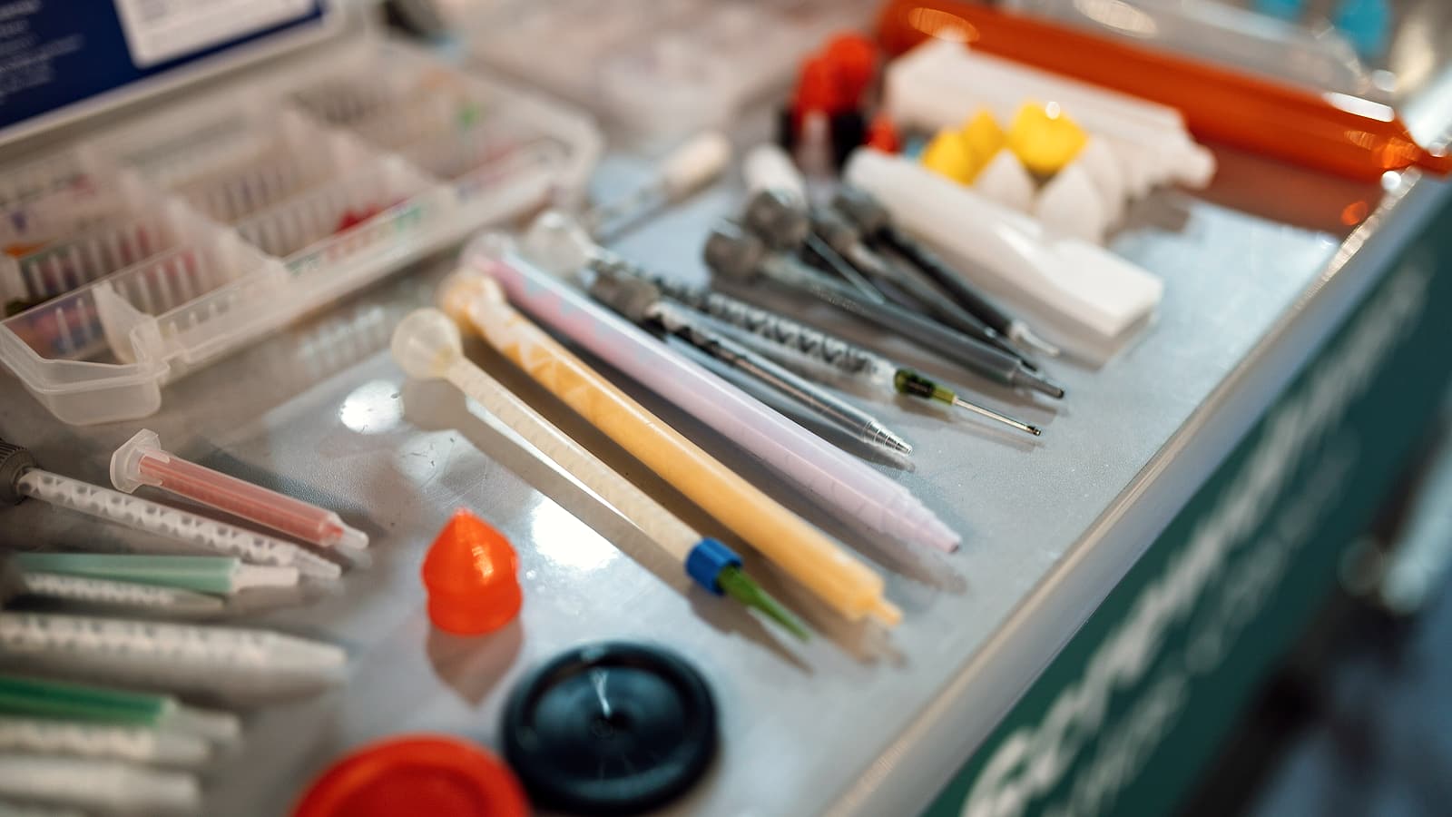 Two people at a workbench in a bright laboratory, one pointing at equipment while the other takes notes.