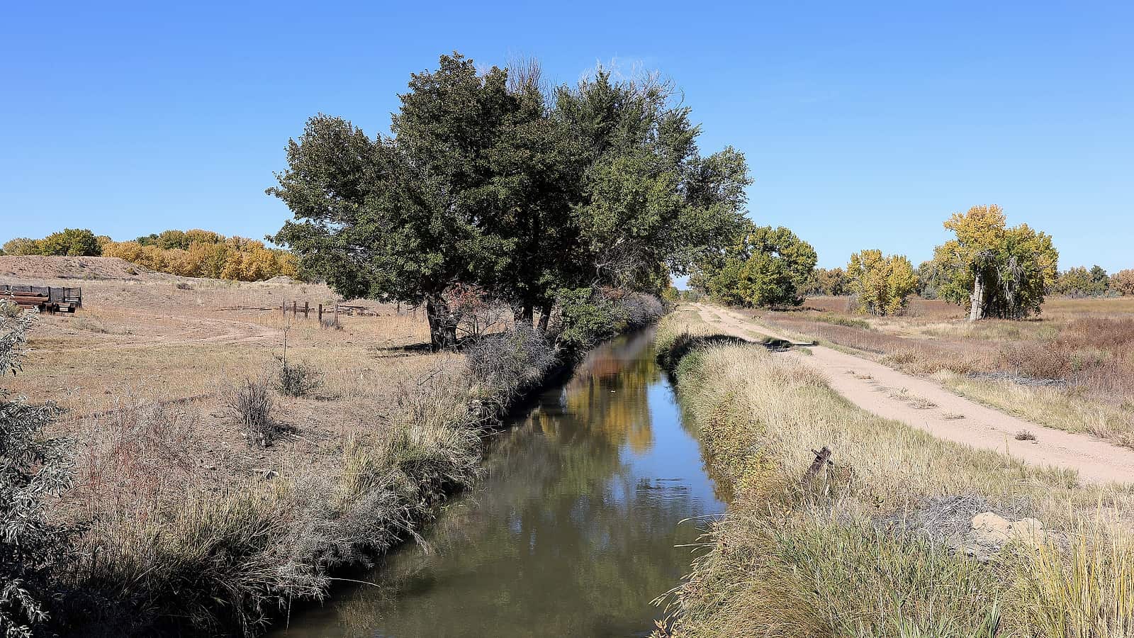 A concrete headgate on an earthen ditch with water running through it beside a dry field and low hills behind.