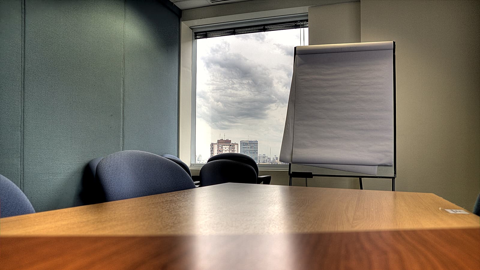 A long conference table with two rows of chairs facing each other, notepads and water glasses set at each place.